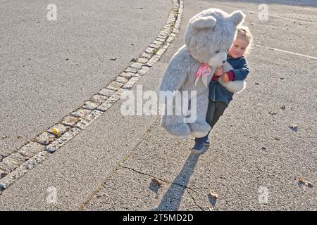 Der starke Beschützer. Das kleine Mädchen mit ihrem großen Stoffbären. Traunstein Bayern Deutschland *** der starke Beschützer das kleine Mädchen mit ihrem großen Stoffbären Traunstein Bayern Deutschland Copyright: XRolfxPossx Credit: Imago/Alamy Live News Stockfoto