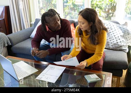 Ernsthaftes vielseitiges Paar, das auf der Couch sitzt und Rechnungen und Finanzen im Wohnzimmer diskutiert Stockfoto