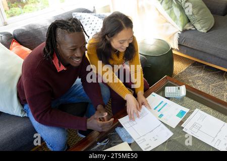 Glückliches, vielfältiges Paar, das auf der Couch sitzt und Rechnungen und inländische Finanzen im Wohnzimmer diskutiert Stockfoto