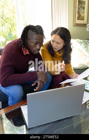 Ernsthaftes, vielseitiges Paar, das mit einem Laptop auf der Couch sitzt und Rechnungen und Finanzen im Wohnzimmer diskutiert Stockfoto