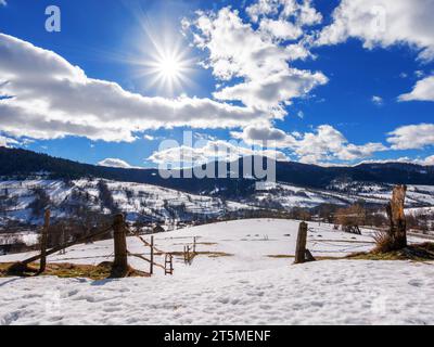 Winterlandschaft mit ländlichem Tal. Bewaldete Berge in der Ferne. Der alte Holzzaun auf dem Hügel. Frostiger und sonniger Tag Stockfoto