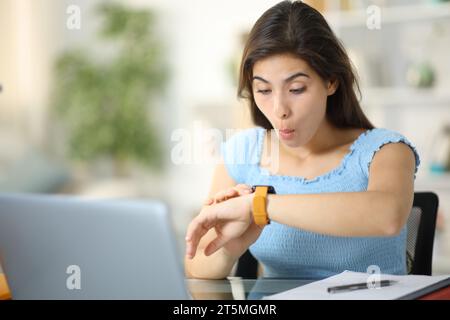 Überraschter Schüler, der zu Hause Smartwatch überprüft Stockfoto