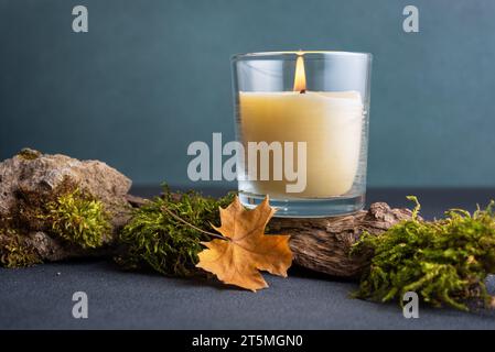 Stillleben mit brennender Kerze im Glasgefäß auf hölzernem Podium mit gefallenen Blättern für die Herbstdekoration Stockfoto