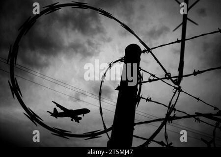 Flughafensicherheit: Flacher Blick auf ein fliegendes Flugzeug durch Stacheldraht. Stockfoto