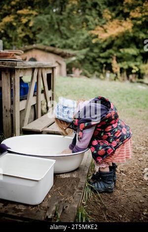 Ein rothaariges Mädchen, das sich für das kalte Wetter zusammengebündelt hat, wäscht sich die Hände in einem Waschbecken. Stockfoto