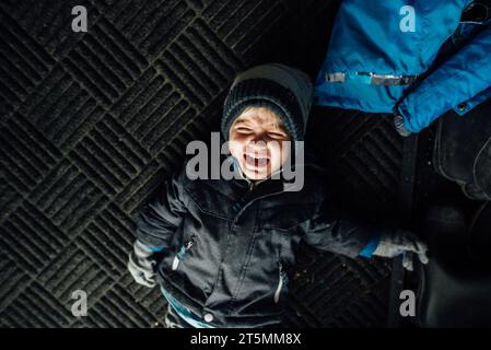 Blick von oben auf den kleinen Jungen, der weint und Wutanfälle auf den Boden wirft Stockfoto