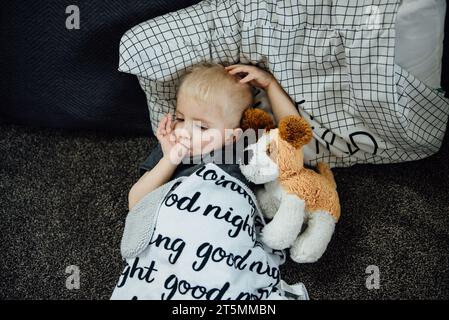 Blick von oben auf den kleinen Jungen, der auf dem Boden lag, mit einem Kissen und einem Stall Stockfoto