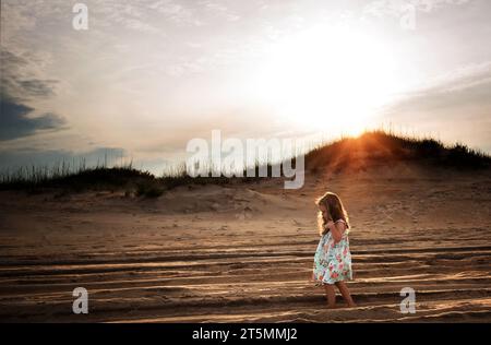 Kleines Mädchen, das bei Sonnenuntergang in Sanddünen läuft Stockfoto