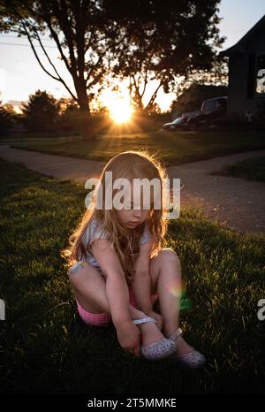 Niedliches kleines Mädchen, das Schuhe im Garten bei Sonnenuntergang anzieht Stockfoto