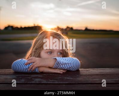 Schönes kleines Mädchen, das sich mit Händen im Gesicht zur Seite sieht Stockfoto