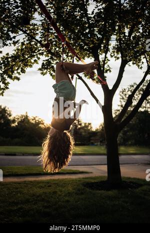 Ein junges Mädchen, das im Sommer kopfüber vom Baum hängt Stockfoto
