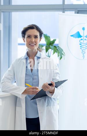 Porträt einer glücklichen kaukasischen Ärztin mit Klemmbrett, die am Rezeptionstresen des Krankenhauses steht Stockfoto