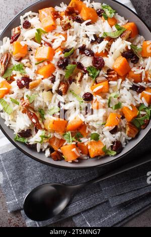 Veganes gewürztes Pilaw mit Süßkartoffeln, Pekannüssen, Zwiebeln und getrockneten Preiselbeeren in einer Schüssel auf dem Tisch. Vertikale Draufsicht von oben Stockfoto