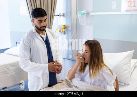Verschiedene männliche Ärzte beobachten Mädchen Patienten mit Asthma Inhalator sitzend im Krankenhausbett Stockfoto