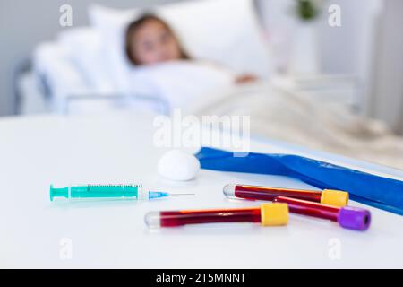 Spritze und Blutproben auf dem Tisch, kaukasische Mädchen Patientin im Krankenhausbett im Hintergrund, Kopierraum Stockfoto