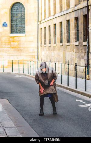 Gebeugte ältere Frau, die mitten in der Rue Mazarine, Paris 6, Frankreich, läuft. Stockfoto