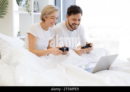 Kaukasier spielt Videospiele, während er zu Hause unter der Decke liegt. Stockfoto
