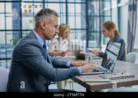 Selbstbewusster Geschäftsmann, der am Konferenztisch in einem modernen Büro sitzt Stockfoto