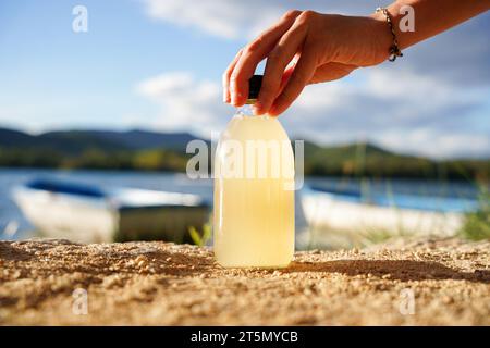 Probiotisches und erfrischendes Zitronengetränk. Hausgemachter fermentierter Kombucha-Tee in einer Glasflasche mit einem See aus Hintergrund. Stockfoto