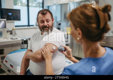 Arzt, der einen kontinuierlichen Blutzuckermessfühler am Arm des Patienten anbringt. Fettleibiger, übergewichtiger Mann besteht das Risiko, an Typ-2-Diabetes zu erkranken. Konzept von Stockfoto