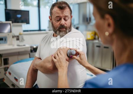 Arzt, der einen kontinuierlichen Blutzuckermessfühler am Arm des Patienten anbringt. Fettleibiger, übergewichtiger Mann besteht das Risiko, an Typ-2-Diabetes zu erkranken. Konzept von Stockfoto