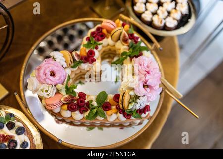 Herzförmiger Kuchen ist luxuriös mit Beeren, Minzblättern, Früchten, Baisons und Creme dekoriert. Stockfoto