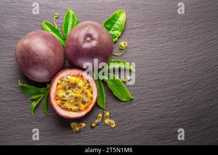 Dunkelviolette Passionsfrüchte und die Hälfte der Maracuya-Frucht isoliert auf Schiefergraphit-grauem Hintergrund. Stockfoto