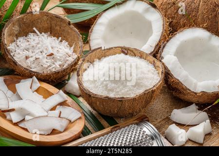 Frisch geöffnete Kokosnüsse zusammen mit Kokosscheiben, Flocken und Kokosblättern auf einem Holztisch. Schöner Hintergrund für Ihre Projekte. Stockfoto