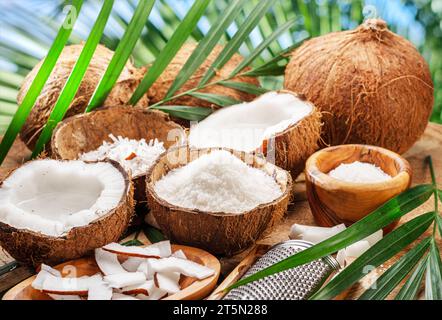 Frisch geöffnete Kokosnüsse zusammen mit Kokosscheiben, Flocken und Kokosblättern auf einem Holztisch. Schöner Hintergrund für Ihre Projekte. Stockfoto