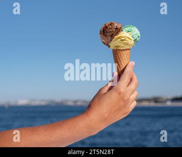 Eiskegel mit bunten Eiskugeln in der Hand auf blauem Himmel Hintergrund. Stockfoto