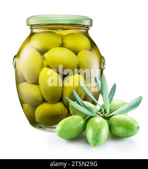 Ganze grüne Oliven, die in Salzlake in der Glasdose gepökelt wurden, und rohe Olivenbeeren in der Nähe. Isoliert auf weißem Hintergrund. Stockfoto