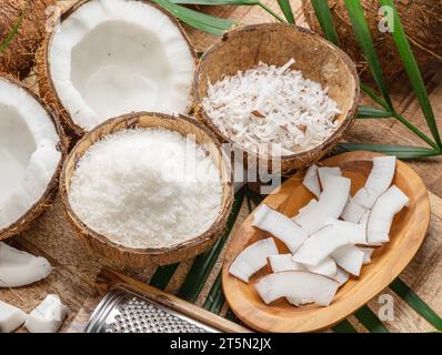 Frisch geöffnete Kokosnüsse zusammen mit Kokosscheiben, Flocken und Kokosblättern auf einem Holztisch. Schöner Hintergrund für Ihre Projekte. Stockfoto