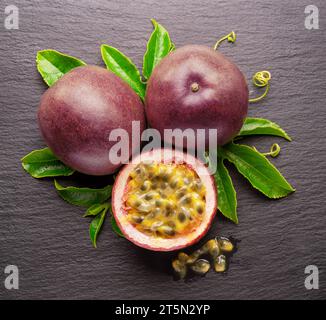 Dunkelviolette Passionsfrüchte und die Hälfte der Maracuya-Frucht isoliert auf Schiefergraphit-grauem Hintergrund. Stockfoto