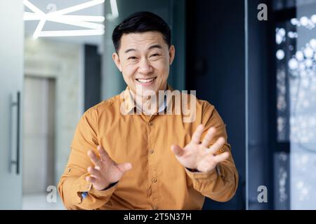 Fröhlicher, erfolgreicher Geschäftsmann, der in der Webkamera zusieht, lächelnder Mann, der mit Kollegen aus der Ferne über Videoanrufe auf einem Laptop spricht, asiatischer Mann am Arbeitsplatz im Büro. Stockfoto