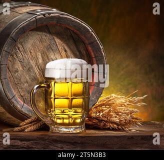 Tasse gekühltes Bier, Weizenohren und Holzbierfässer auf dem Holztisch. Stockfoto