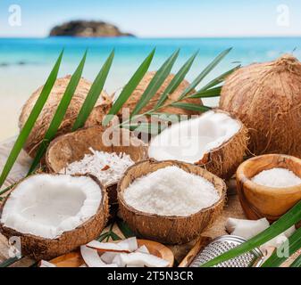 Frisch geöffnete Kokosnüsse zusammen mit Kokosscheiben, Flocken und Kokosblättern auf exotischem Hintergrund. Schöner Hintergrund für Ihre Projekte. Stockfoto