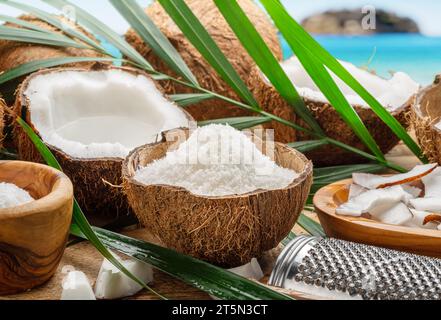 Frisch geöffnete Kokosnüsse zusammen mit Kokosscheiben, Flocken und Kokosblättern auf exotischem Hintergrund. Schöner Hintergrund für Ihre Projekte. Stockfoto