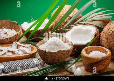 Frisch geöffnete Kokosnüsse zusammen mit Kokosscheiben, Flocken und Kokosblättern auf einem Holztisch. Schöner Hintergrund für Ihre Projekte. Stockfoto
