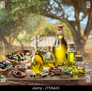 Eine Flasche handgefertigtes Olivenöl steht auf einem Holztisch, hinter einem Olivengarten an einem etwas Bokeh, sonnigen Tag. Stockfoto