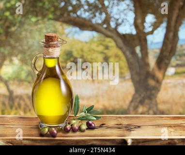 Eine Flasche handgefertigtes Olivenöl steht auf einem Holztisch, hinter einem Olivengarten an einem etwas Bokeh, sonnigen Tag. Stockfoto