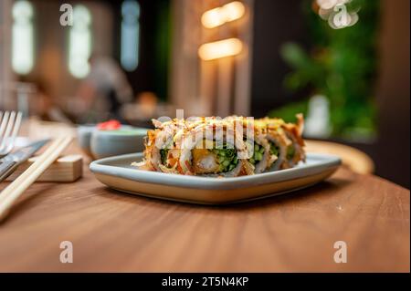 Sushi-Rolle mit Thunfischflocken, Tempura-Garnelen, Mango und Gurke auf einem Teller Stockfoto