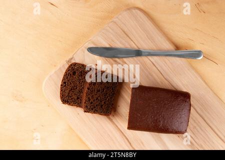 Dunkles Brot in Brotform und in Scheiben geschnitten auf hellbeigem Holzhintergrund Stockfoto