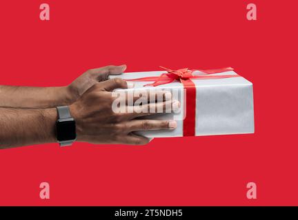 Hand eines Afro-Mannes, der eine Geschenkbox über isoliertem roten Hintergrund hält. Stockfoto
