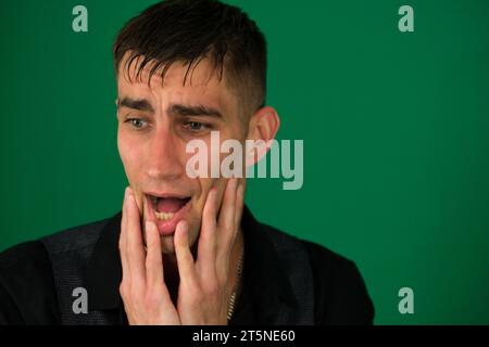 Emotionen eines gutaussehenden Mannes auf grünem Hintergrund Chromakey Nahaufnahme dunkles Haar junger Mann netter Mann in einem schwarzen Hemd mit dem Bart posiert lustige Gesichter. Hochwertige Fotos Stockfoto