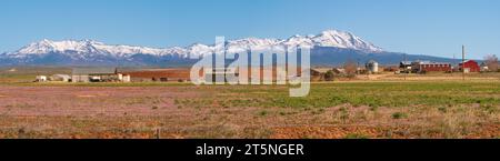 Panorama einer typischen Farm und Scheune im Westen der USA mit schneebedeckten Bergen im Hintergrund, im Frühjahr, Utah, USA. Stockfoto