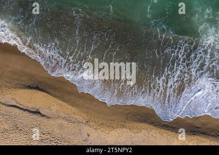 Blick aus der Vogelperspektive auf die Meereswellen, die einen abgelegenen Sandstrand waschen Stockfoto