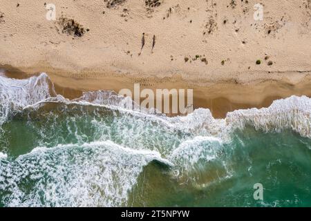Blick aus der Vogelperspektive auf die Meereswellen, die einen abgelegenen Sandstrand waschen Stockfoto