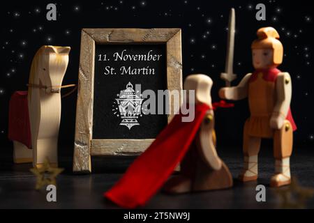 Augsburg, Bayern, Deutschland - 6. November: St. Martin mit seinem Pferd und einem roten Umhang vor einem Bettler neben einer Tafel mit Aufschrift: 11. November St. Martin FOTOMONTAGE *** St. Martin mit seinem Pferd und einem roten Mantel vor einem Bettler neben einer Tafel mit der Inschrift: 11. November St. Martin FOTOMONTAGE Credit: Imago/Alamy Live News Stockfoto