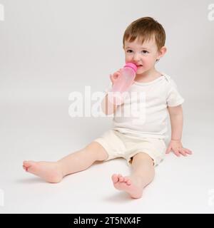 Happy Baby trinkt Milch aus der Flasche auf weißem Studiohintergrund. Ruhendes Kind isst Formel. Kind etwa zwei Jahre alt (ein Jahr neun Monate) Stockfoto