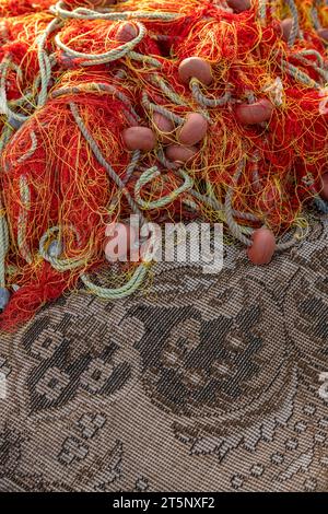 Alte entsorgte griechische Fischernetze, die auf einem östlichen Teppich am Hafen liegen, in einer abstrakten Komposition, die als Hintergrund verwendet werden kann. Stockfoto